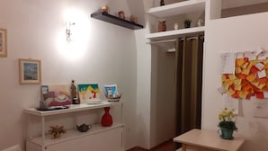 A small, well-lit room with a white desk, a chair, and a shelf with various decorative items. There is a door with a curtain, and a wall with a bulletin board. - casa normanna (Salerno)