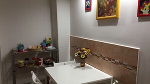 A small dining area with a white table and chairs, a vase with flowers, and a shelf with various items including a coffee can. - casa normanna (Salerno)