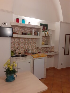 A compact kitchen with white cabinets, a built-in oven, and a small sink. There is a TV mounted on the wall above the counter. - Casa Normanna (Salerno)