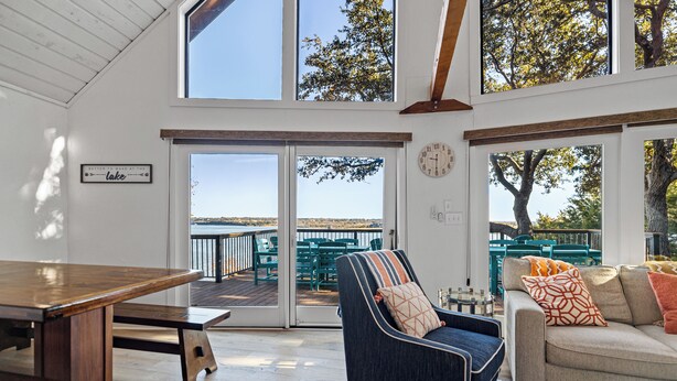 Una habitación amplia con una mesa de comedor de madera, un sillón azul y un sofá beige. Hay un ventanal con vistas al exterior.