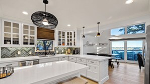 Una cocina moderna con armarios blancos, una isla grande y vistas al exterior a través de amplios ventanales.