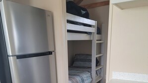 Et lille køkken med et rustfrit stål køleskab, en trækøjeseng og en hvid bordplade.