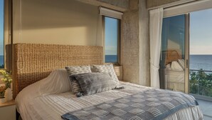 Ein Schlafzimmer mit einem großen Bett, einem gewobenen Kopfteil und Blick auf den Ozean durch eine Schiebetür.