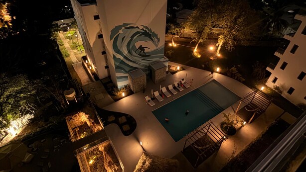 Ein Hotel mit einer großen Wandmalerei, die eine Welle zeigt, einem Schwimmbad und Sitzgelegenheiten im Freien.
