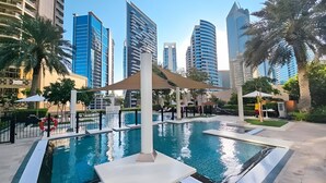 Piscina con una sombrilla, rodeada de palmeras y edificios modernos.