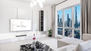 Una sala de estar moderna con una gran pantalla de televisión mostrando 'GemStay', un sofá, una mesa de centro y vistas de un paisaje urbano a través de grandes ventanales.