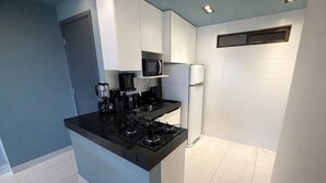 Une cuisine moderne dotée d’un plan de travail noir, d’une cuisinière à gaz, d’un four à micro-ondes, d’une machine à café et d’un réfrigérateur.