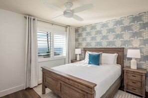 Een slaapkamer met een houten bed, twee nachtkastjes met lampen, een plafondventilator, een raam met jaloezieën en behang met een patroon.