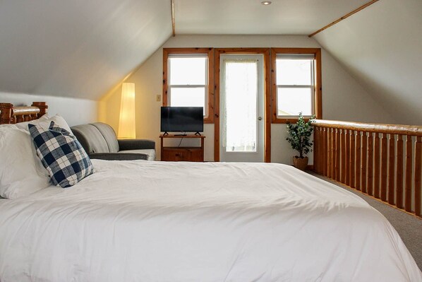 A bedroom with a large bed, a television on a wooden stand, and a window with a view.