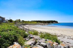Una playa costera con un paseo de madera, casas y un litoral rocoso.