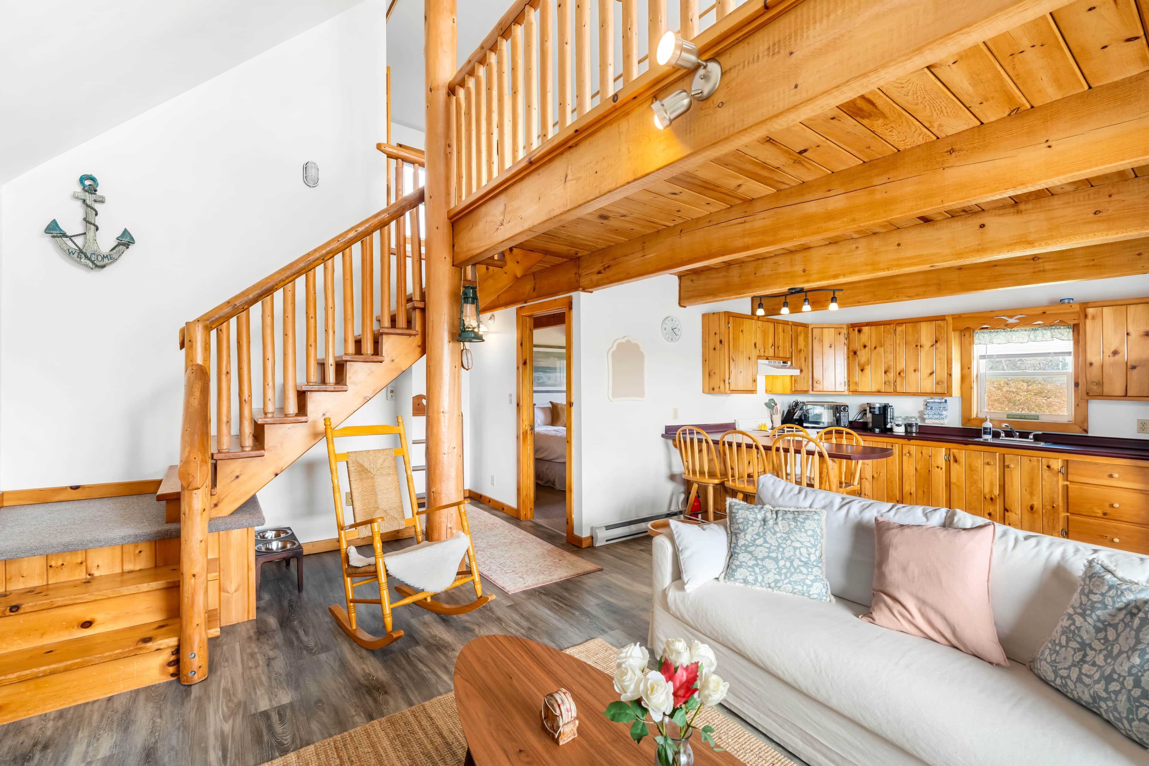 A wooden interior with a staircase, a living room with a sofa, a kitchen area, and a dining table.