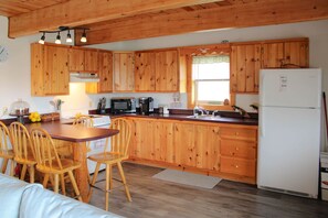 Una cocina con armarios de madera, un refrigerador blanco, una estufa y un comedor con sillas de madera.