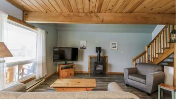 Un salon chaleureux avec un plafond en bois, une télévision, une cheminée et un escalier.