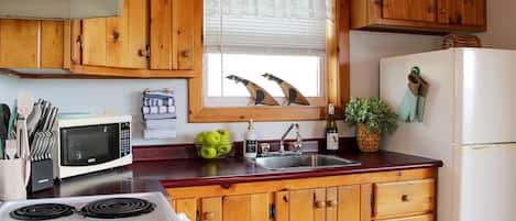 A kitchen with wooden cabinets, a microwave, a stove, a sink, and a window with decorative items.