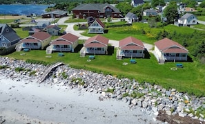A coastal residential area with houses featuring gabled roofs and front porches, a rocky shoreline, and a clear view of the water.