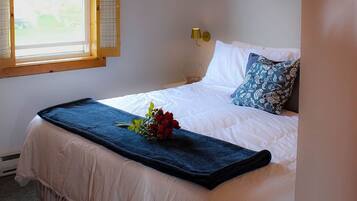 A bedroom with a bed, a window, a wall-mounted lamp, and a framed picture.