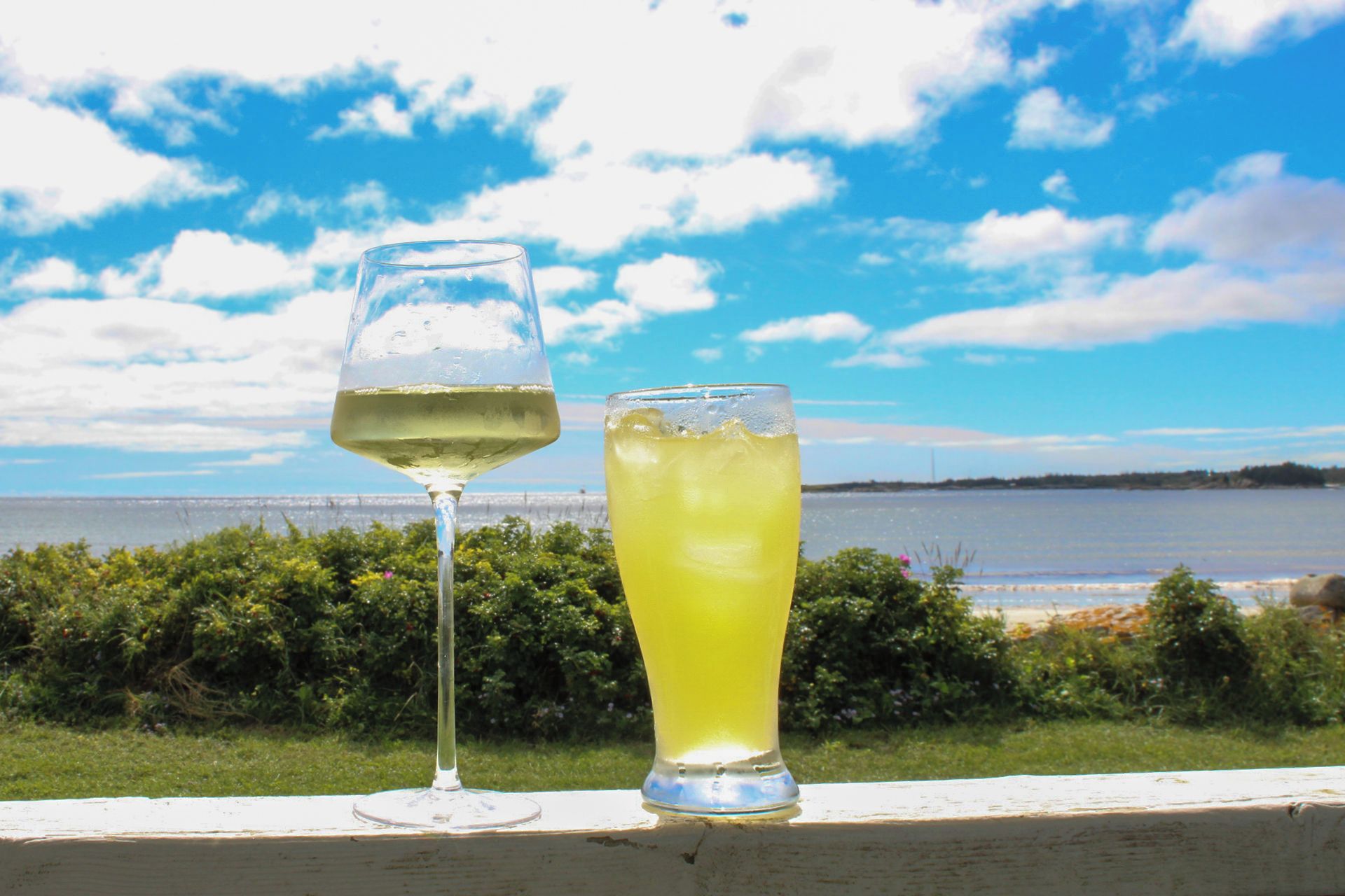Twee glazen dranken op een rand met uitzicht op water en lucht.