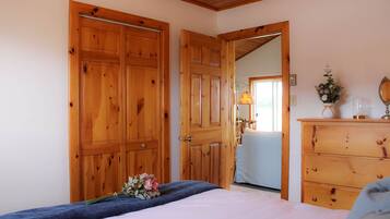 A bedroom with a wooden wardrobe, a dresser, a bed with a blue blanket, and a bouquet of flowers.