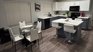 A modern kitchen with white cabinets, a black microwave, and a dining area with a glass table and white chairs. - Avondale Retreat with Pool near Stadium, Top Golf and Spring Training (Avondale)