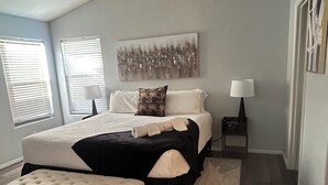 A bedroom with a bed, a ceiling fan, a nightstand, a lamp, and a window with blinds. - Avondale Retreat with Pool near Stadium, Top Golf and Spring Training (Avondale)