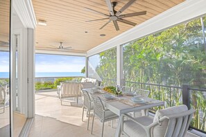 A dining area with a table set for four, large windows, and ceiling fans. - A Captiva Island Luxury Estate With Panoramic Gulf Views and Private Oasis (Captiva)