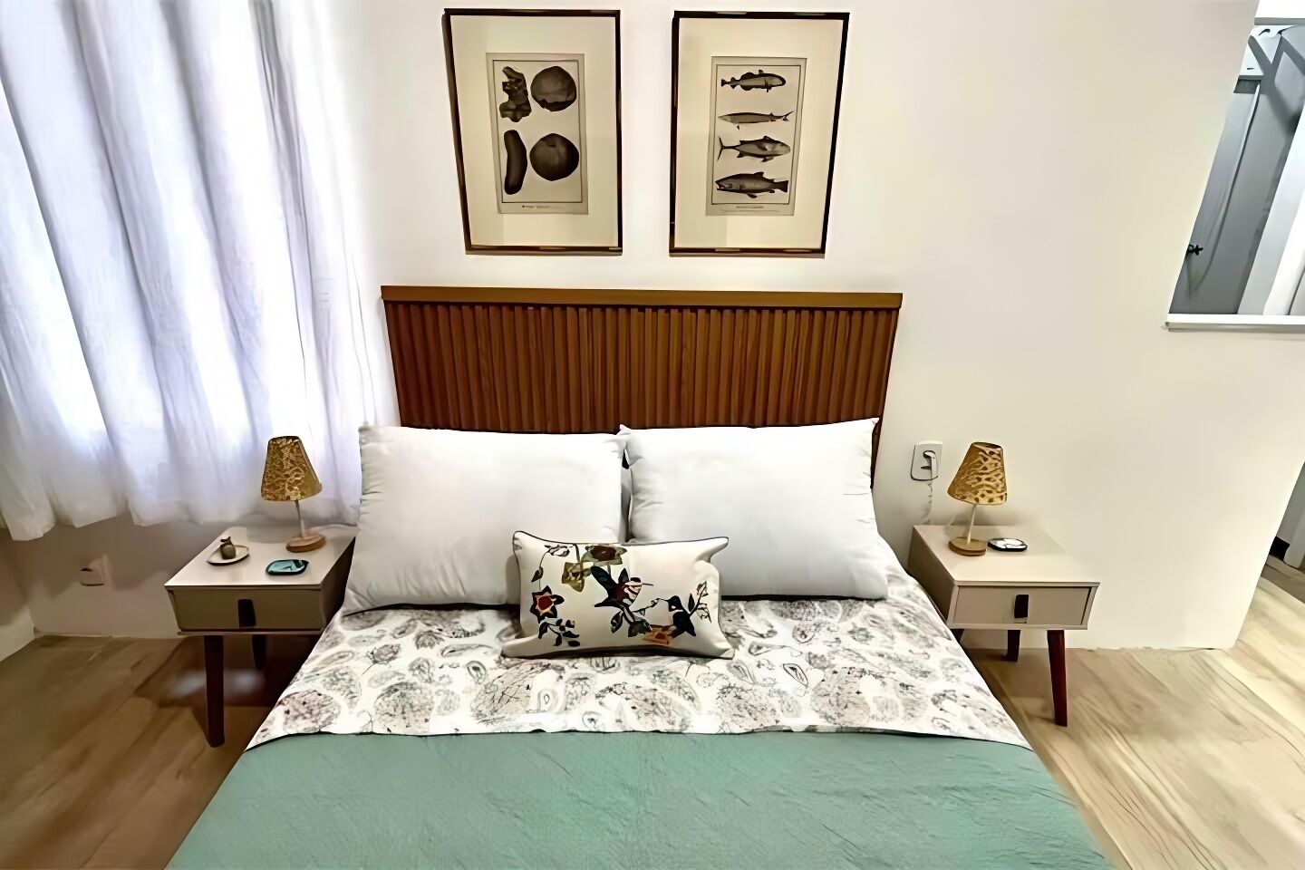 A neatly arranged bedroom with a wooden headboard, two bedside tables with lamps, a floral pillow, and framed fish illustrations on the wall.
