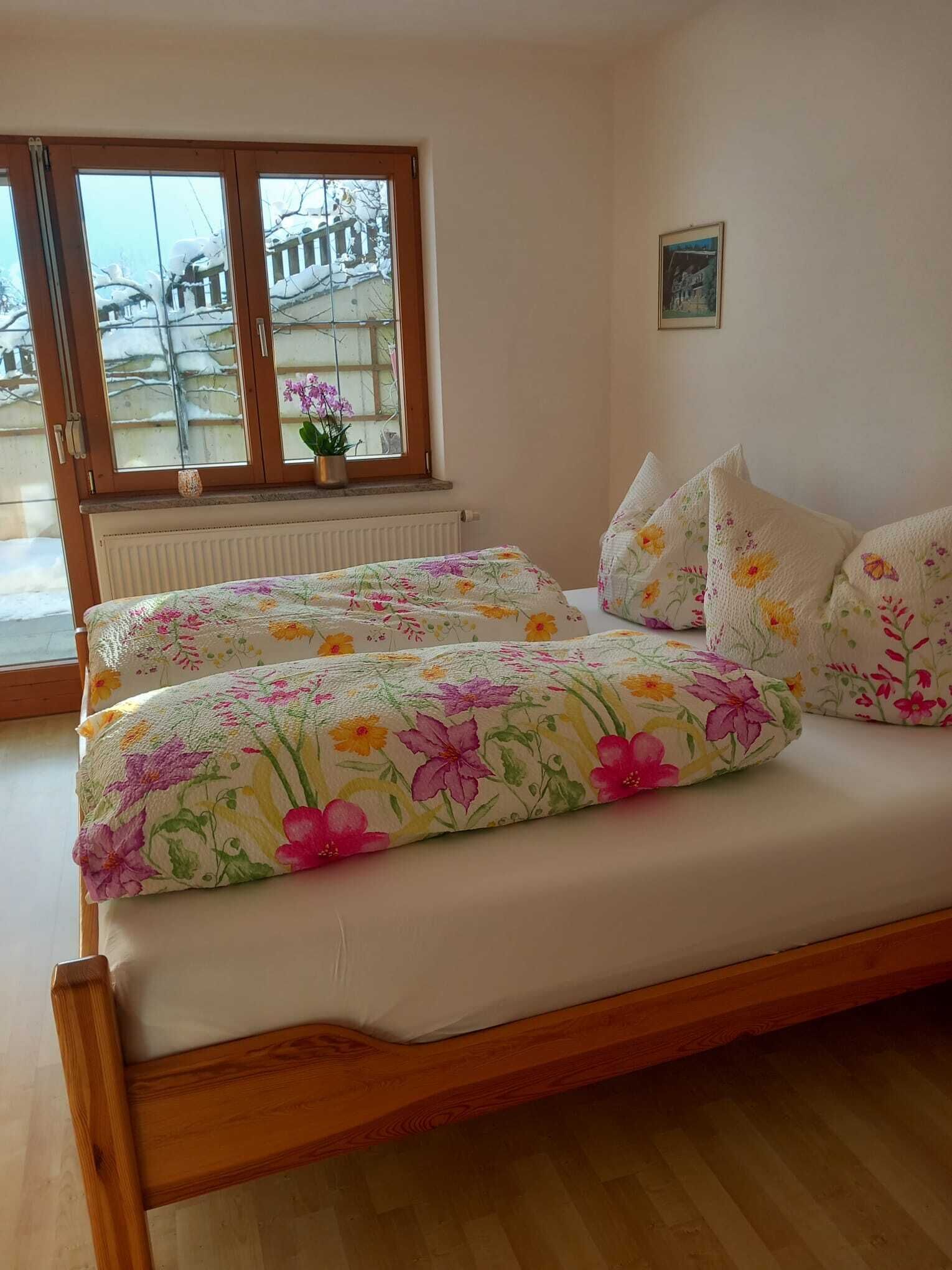 A bedroom with a wooden bed, floral bedding, a window with a view of a snowy landscape, and a radiator.