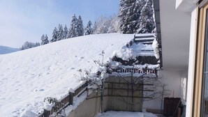 A snow-covered outdoor area with a wooden fence, a concrete pathway, and a building with a stone wall and a window. - House at the edge of the forest Thiersee (Thiersee)