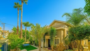 Il s’agit d’une propriété résidentielle dotée d’un jardin bien entretenu, d’un court de tennis et d’une maison à deux étages dont la façade est de couleur beige.