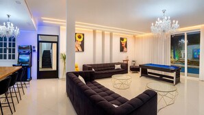 Un salon moderne avec un canapé d’angle, une table de billard et un espace dédié aux jeux vidéo avec une console.
