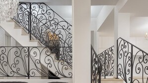 Un intérieur moderne avec un escalier orné de rampes en métal noir, deux fauteuils noirs capitonnés et une table en verre transparent.
