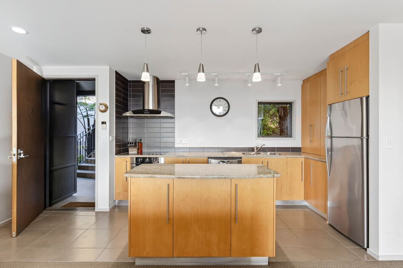 A modern kitchen with wooden cabinets, stainless steel appliances, and pendant lighting.