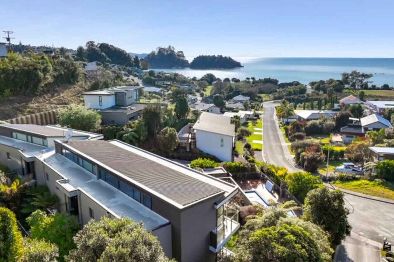 A residential area with modern houses, a road, and a view of the sea.