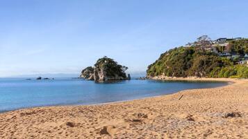 A sandy beach with footprints, a calm sea, and a rocky island with trees.