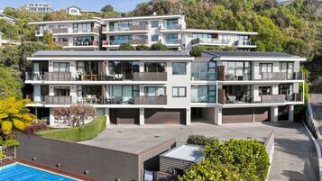 A multi-story residential building with balconies, a swimming pool, and a view of a hilly landscape.