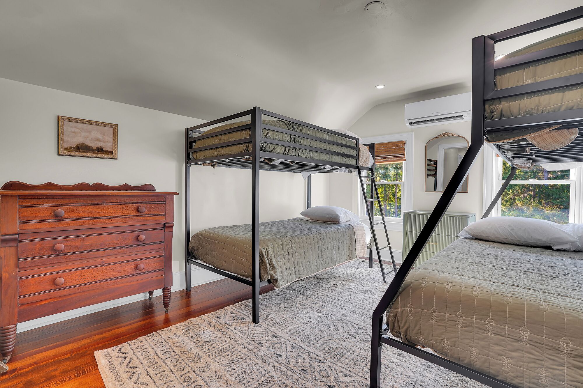Une chambre avec un lit superposé, une commode en bois et un tapis à motifs.
