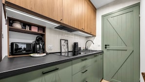 Uma cozinha com armários de madeira, bancada preta, torradeira Bosch, máquina de café e porta verde.