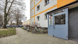 Um edifício com porta azul, bicicletas estacionadas e um estacionamento com carros.