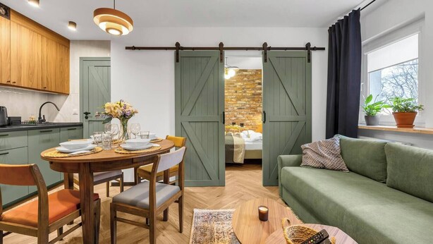 Uma sala de estar aconchegante com uma mesa de jantar posta para quatro pessoas, um sofá verde e uma porta de celeiro deslizante que dá para um quarto.