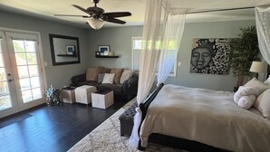 Un dormitorio con cama con dosel, ventilador de techo, ventana grande y vistas al exterior.