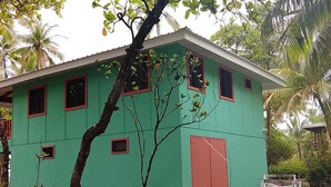 Un bâtiment écologique doté de nombreuses fenêtres et d’une porte rouge, entouré d’arbres et de feuillage.