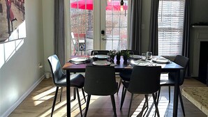 A dining area with a table set for four, chairs, a potted plant, and a view through a window with curtains. - King Bed, Workspace, Games near RDU, RTP, Downtown (Raleigh)
