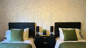 A double bed with green bedding, a black nightstand with a lamp, and a wall with a leaf pattern. - King Bed, Workspace, Games near RDU, RTP, Downtown (Raleigh)