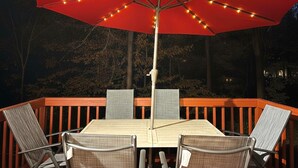 A deck with a table and four chairs, an umbrella with string lights, and a wooden railing. - King Bed, Workspace, Games near RDU, RTP, Downtown (Raleigh)
