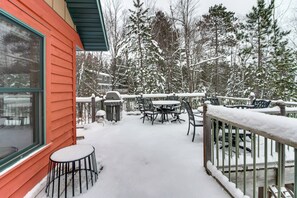 Une terrasse enneigée, dotée de mobilier d’extérieur, d’un barbecue et offrant une vue sur une zone boisée.