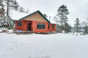 Une cabane rouge, dont le toit est recouvert de neige, entourée d’arbres.
