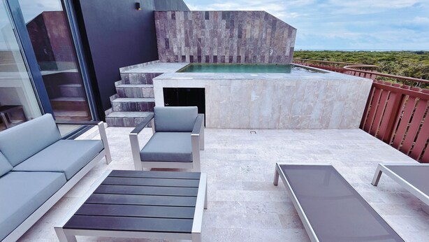 Un patio exterior moderno con piscina, mobiliario y una escalera que sube a un nivel superior.