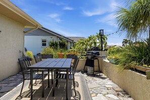 Eine Terrasse im Freien mit Tisch, Stühlen, einem Grill und Pflanzkübeln.