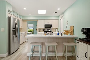 A modern kitchen with a central island, bar stools, a refrigerator, and a coffee machine. - Canal-Front Pool Home Near Gulf Beaches & Golf (Rotonda West)