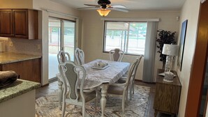 A dining area with a table set for four, surrounded by white chairs with cushioned seats. A ceiling fan is visible above the table, and a window provides natural light. - Serene 3-bedroom house in Sun City
Golf course & lake front near Stadium. (Sun City)